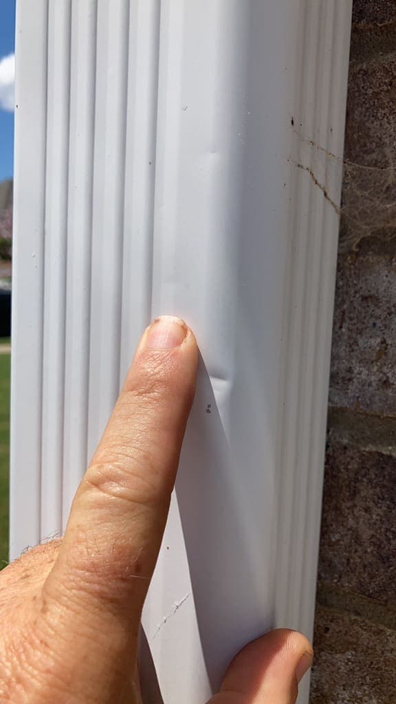 Finger pointing at a hail dent in an aluminum downspout