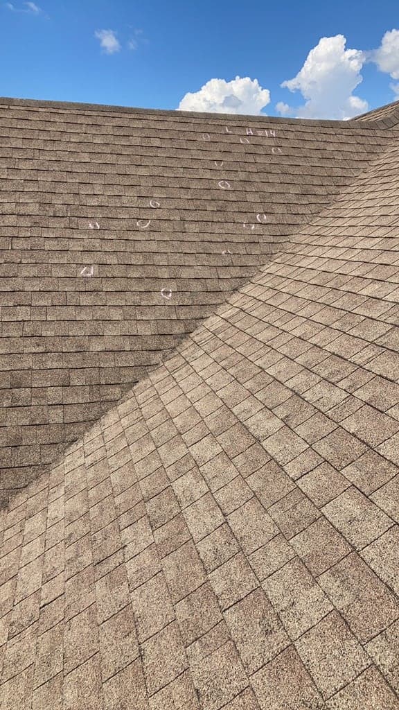 Wide view of an asphalt shingle slope with many separate hail strikes marked in chalk