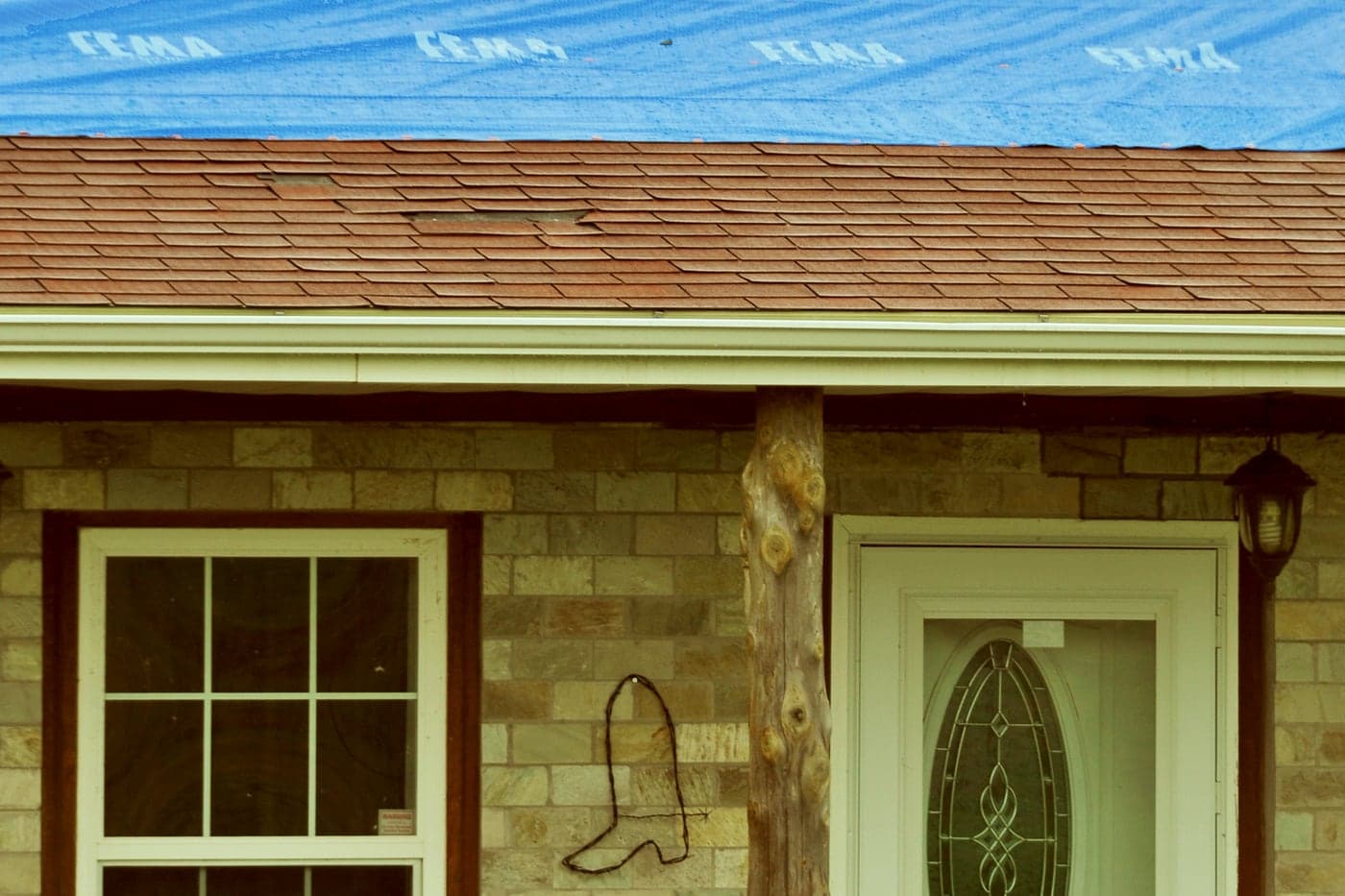 House with a tarp covering the upper roof slope and damaged shingles visible below it