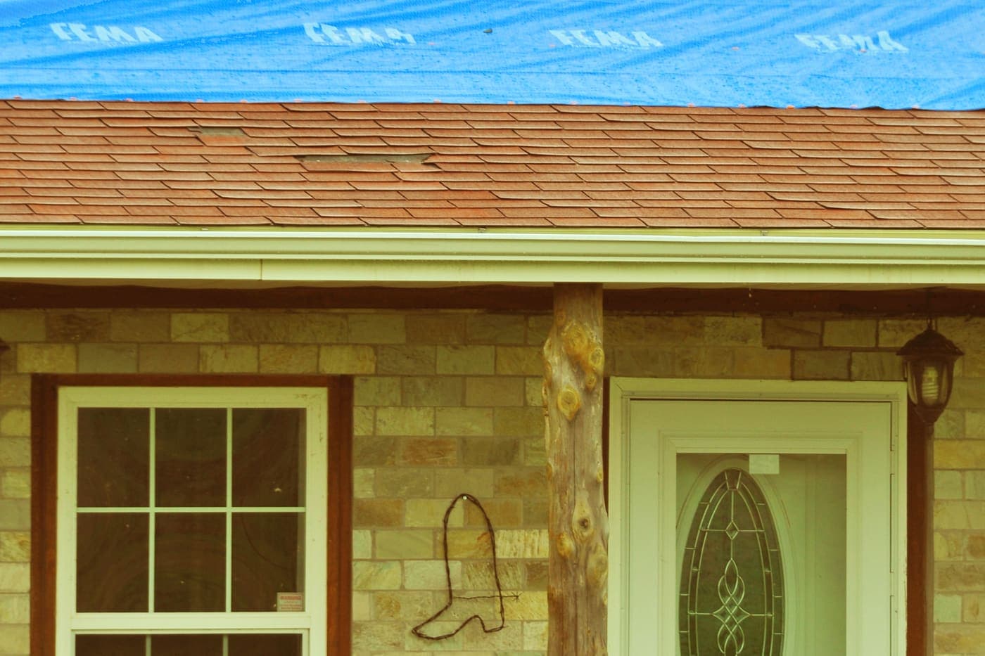 Blue emergency tarp covering the damaged upper section of a shingle roof
