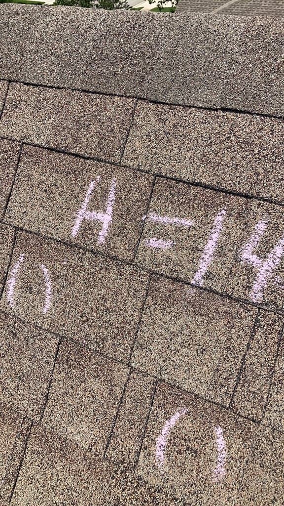 Chalk marking reading A = 14 on an asphalt shingle slope with individual hail hits circled