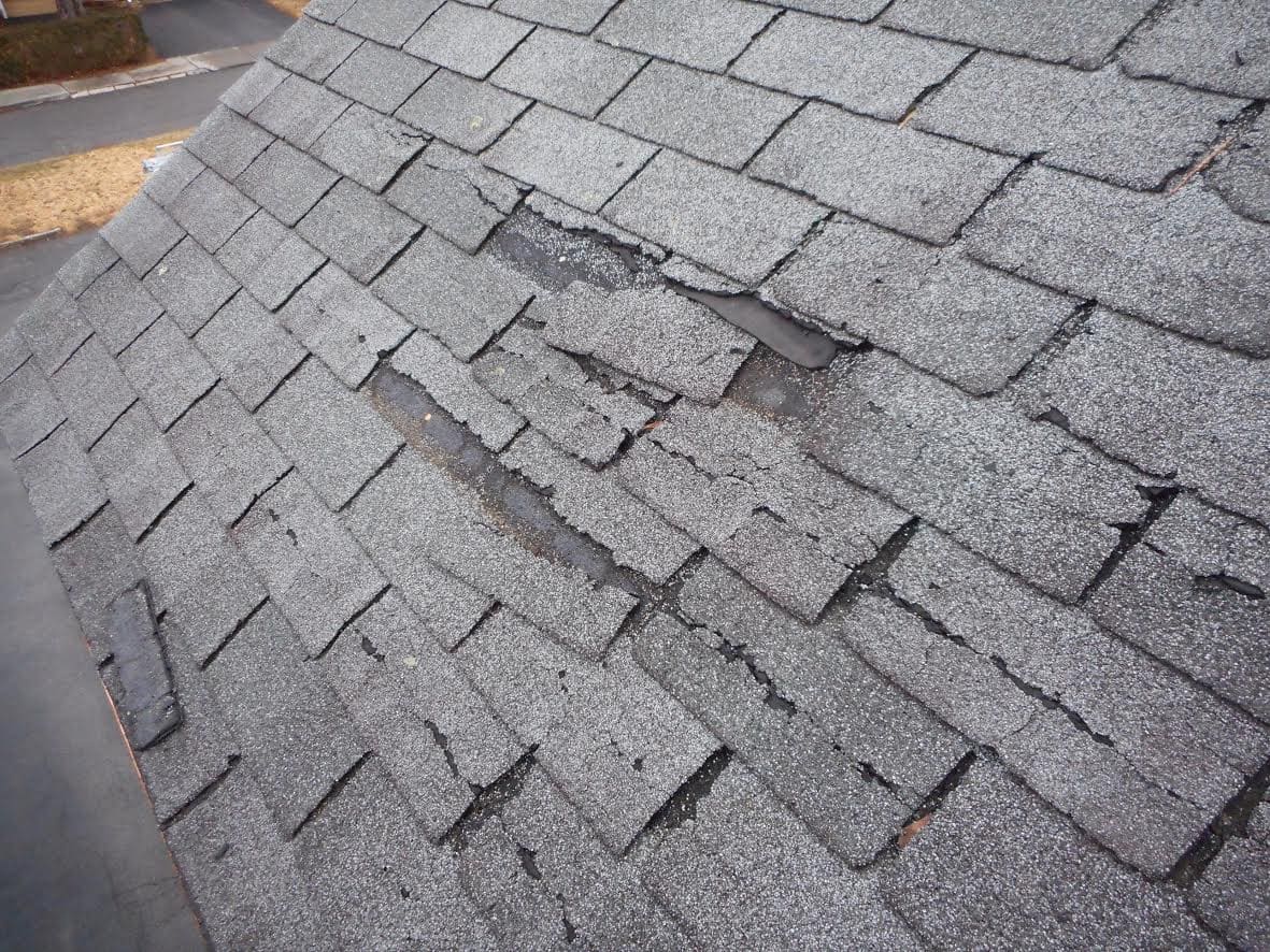 Asphalt shingle roof with torn tabs and exposed underlayment after storm damage