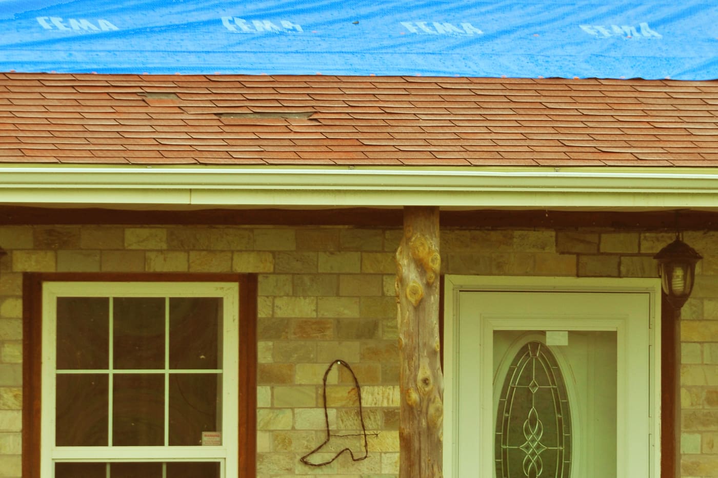 Blue emergency tarp covering the damaged upper section of a shingle roof